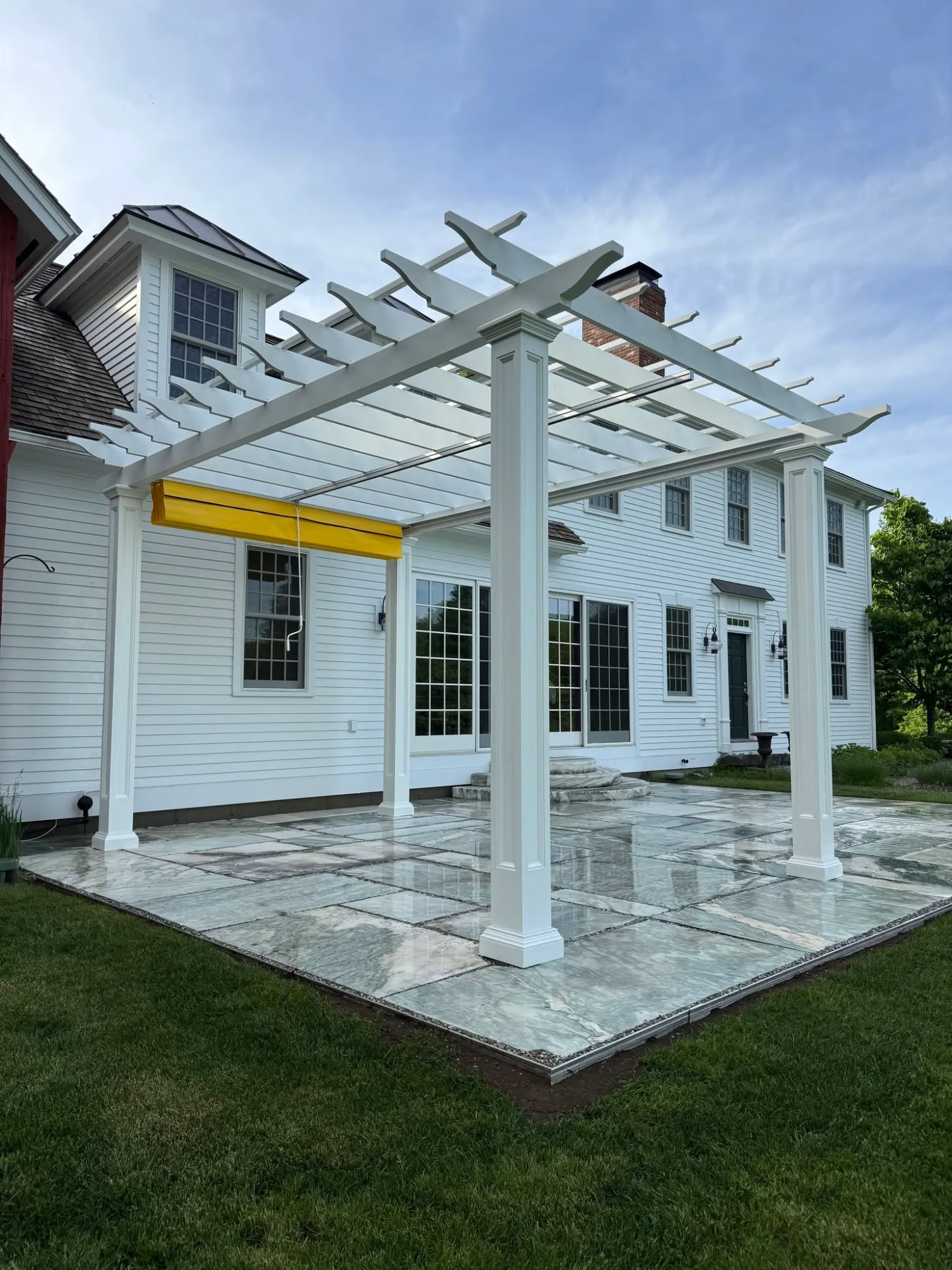 White pergola with retractable shade over a natural stone patio built by Apex Land and Construction